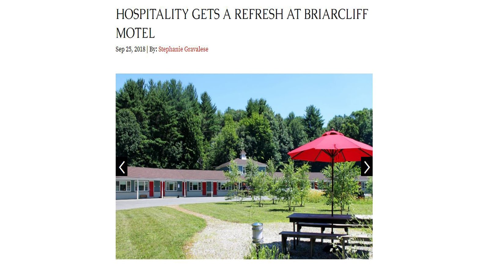 A sunny view of Briarcliff Motel, a pet-friendly motel with a row of rooms and a red umbrella over a table in a green grassy area.