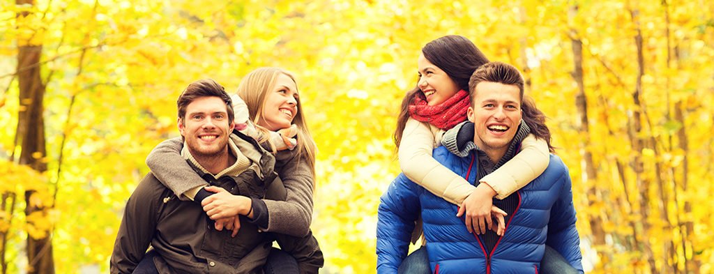 Two couples enjoying a piggyback ride in a forest with vibrant autumn foliage near a pet-friendly motel in the Berkshires.