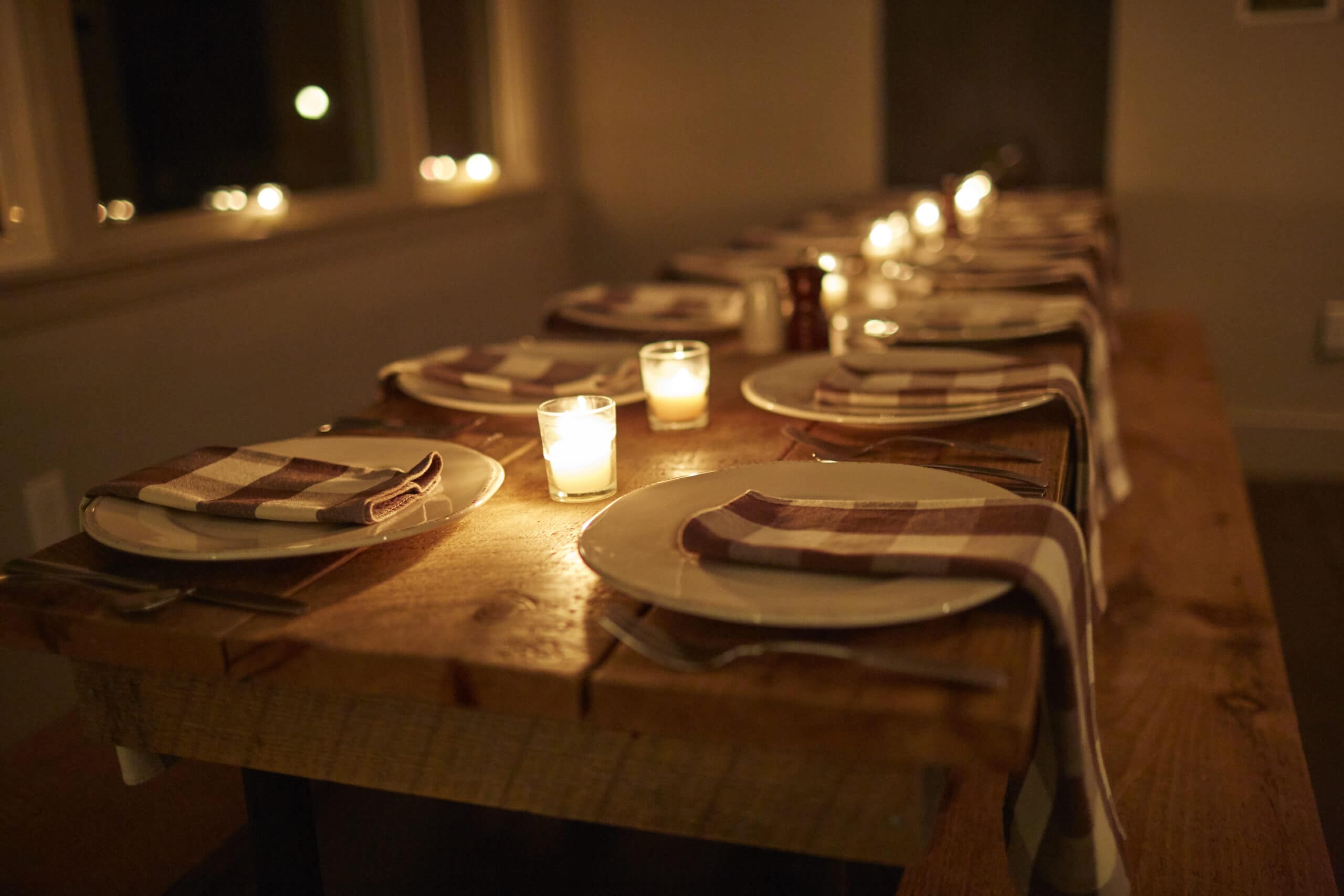 A dimly lit dining table set with white plates, checkered napkins, and lit candles in a cozy Berkshires motel, creating a welcoming ambiance.