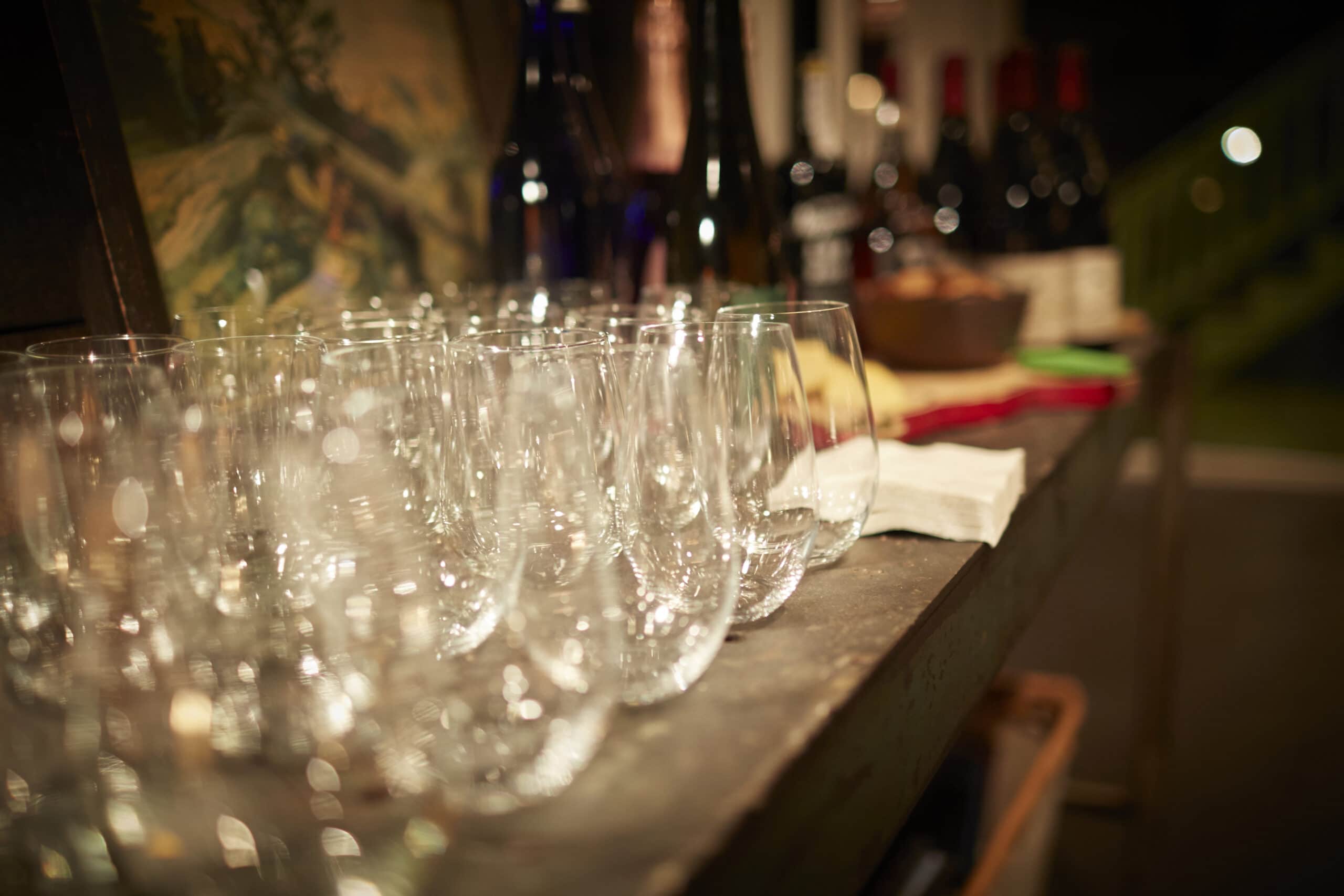 Row of empty wine glasses on a wooden bar in a Berkshires motel, with bottles and blurred background indoor setting.